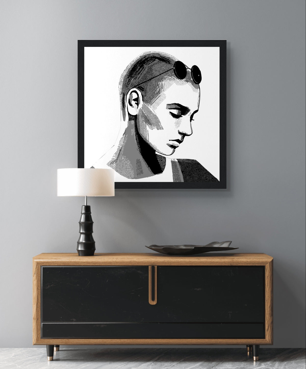 Sinéad O'Connor portrait print in a black frame above a black and wood sideboard with a table lamp