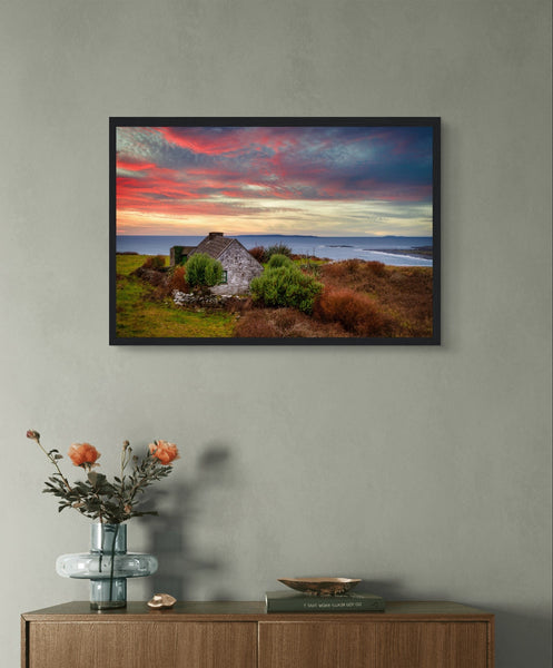 Art print: Serene sunset over Atlantic Ocean, Doolin, Co. Clare, Ireland. Small cottage nestled amid coastal cliffs, vibrant sky in hues of orange and pink, capturing tranquil beauty of Irish countryside.