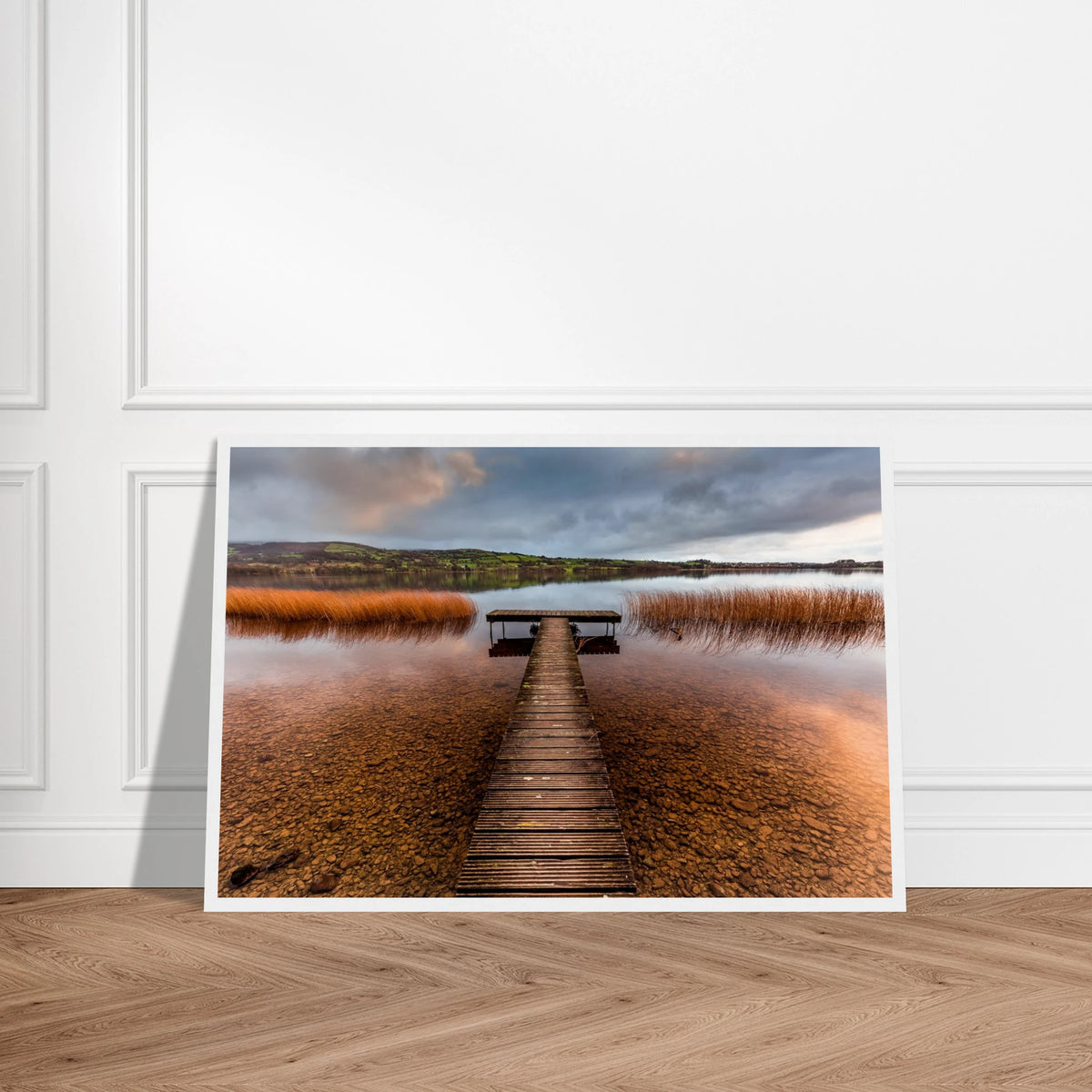 Old Jetty, Lough Derg photographic print, wooden jetty through golden reeds, white frame leaning on a panelled wall