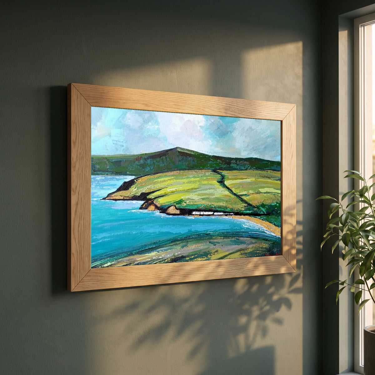 Cushendun framed print in a natural oak frame on a dark green wall beside a window, dappled plant shadow