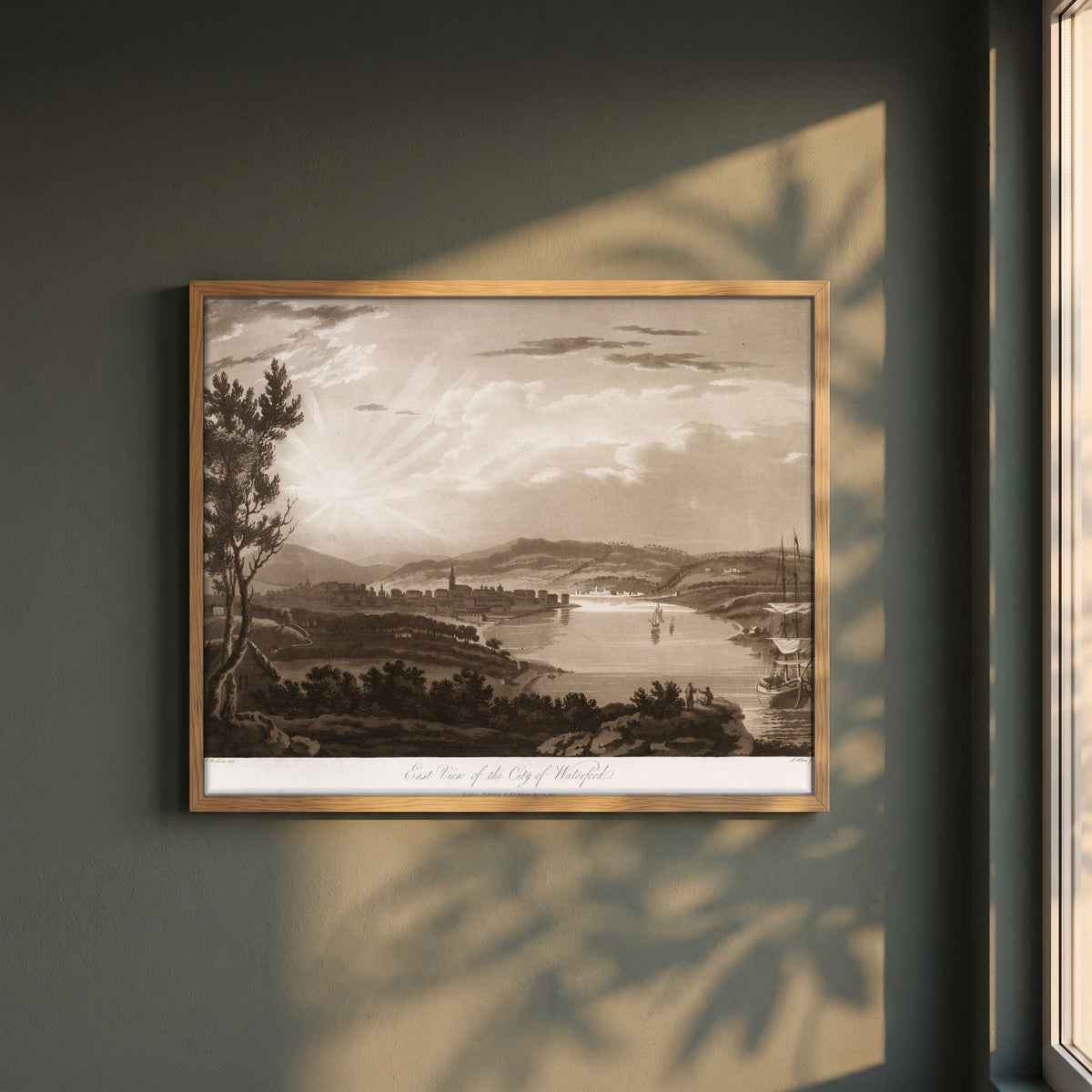 East View of the City of Waterford by Thomas Sautelle Roberts Art Print framed print in a natural oak frame on a dark green wall beside a window, dappled plant shadow
