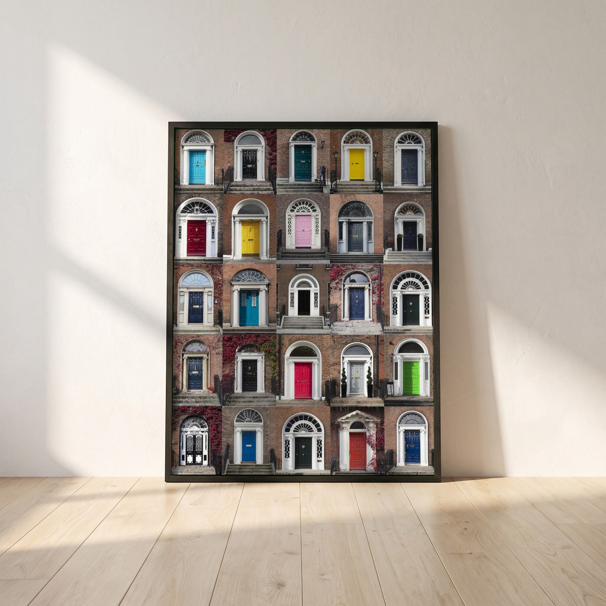 Framed Doors of Dublin framed print in a black frame leaning against a white plaster wall on oak floorboards in morning light