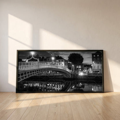 Night View of Ha'penny Bridge framed print in a black frame leaning against a white plaster wall on oak floorboards in morning light