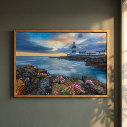 Hook Head Lighthouse, Wexford framed print in a natural oak frame on a dark green wall beside a window, dappled plant shadow