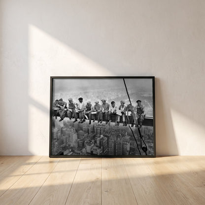 Lunch Atop a Skyscraper framed print in a black frame leaning against a white plaster wall on oak floorboards in morning light