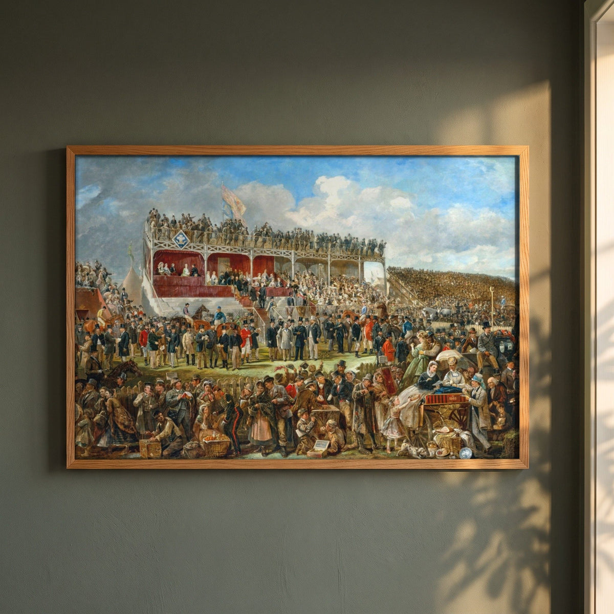 Punchestown Races by John Fergus O'Hea framed print in a natural oak frame on a dark green wall beside a window, dappled plant shadow