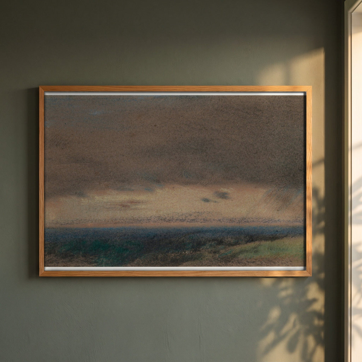 Stormy Clouds at Sunrise framed print in a natural oak frame on a dark green wall beside a window, dappled plant shadow
