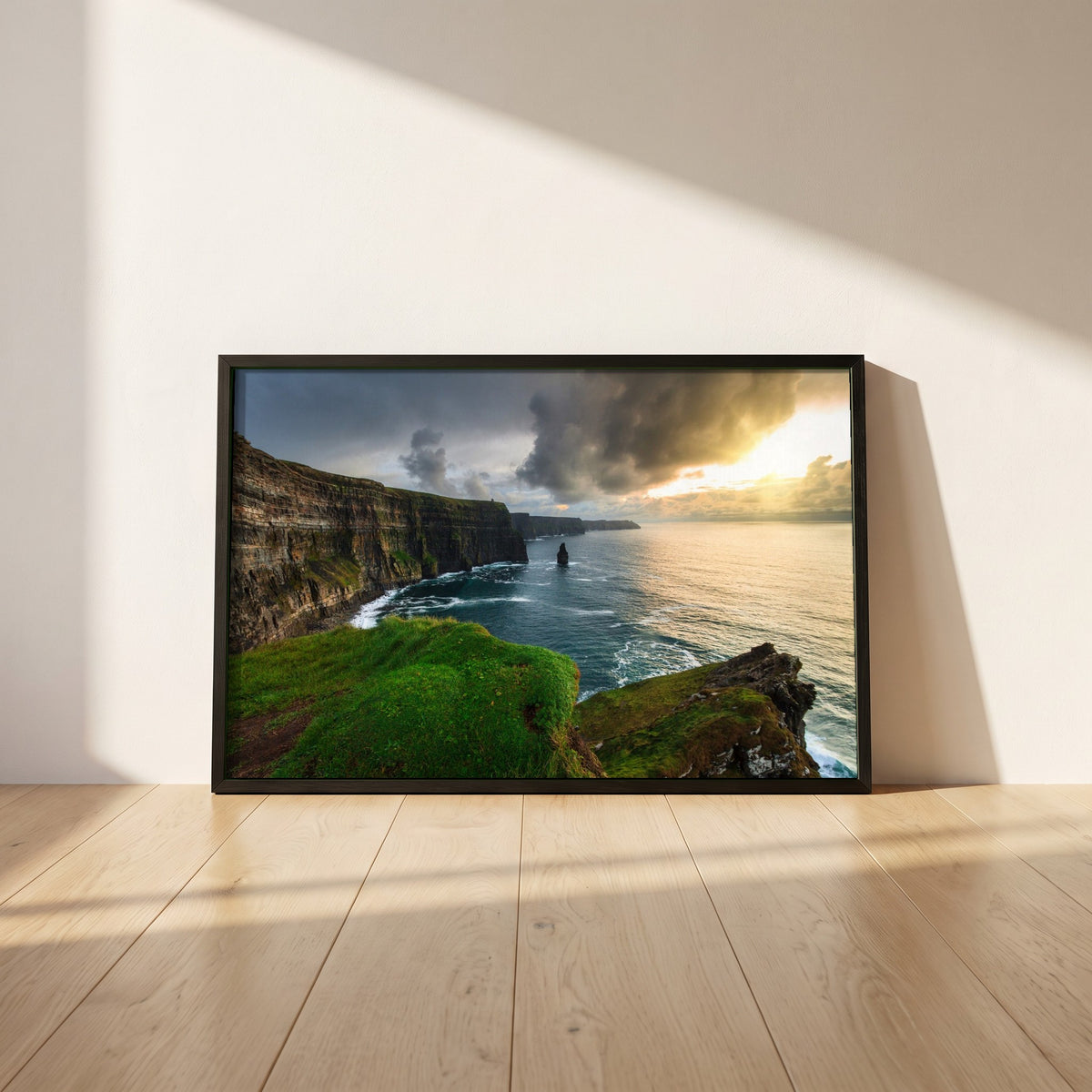 Cliffs of Moher framed print in a black frame leaning against a white plaster wall on oak floorboards in morning light