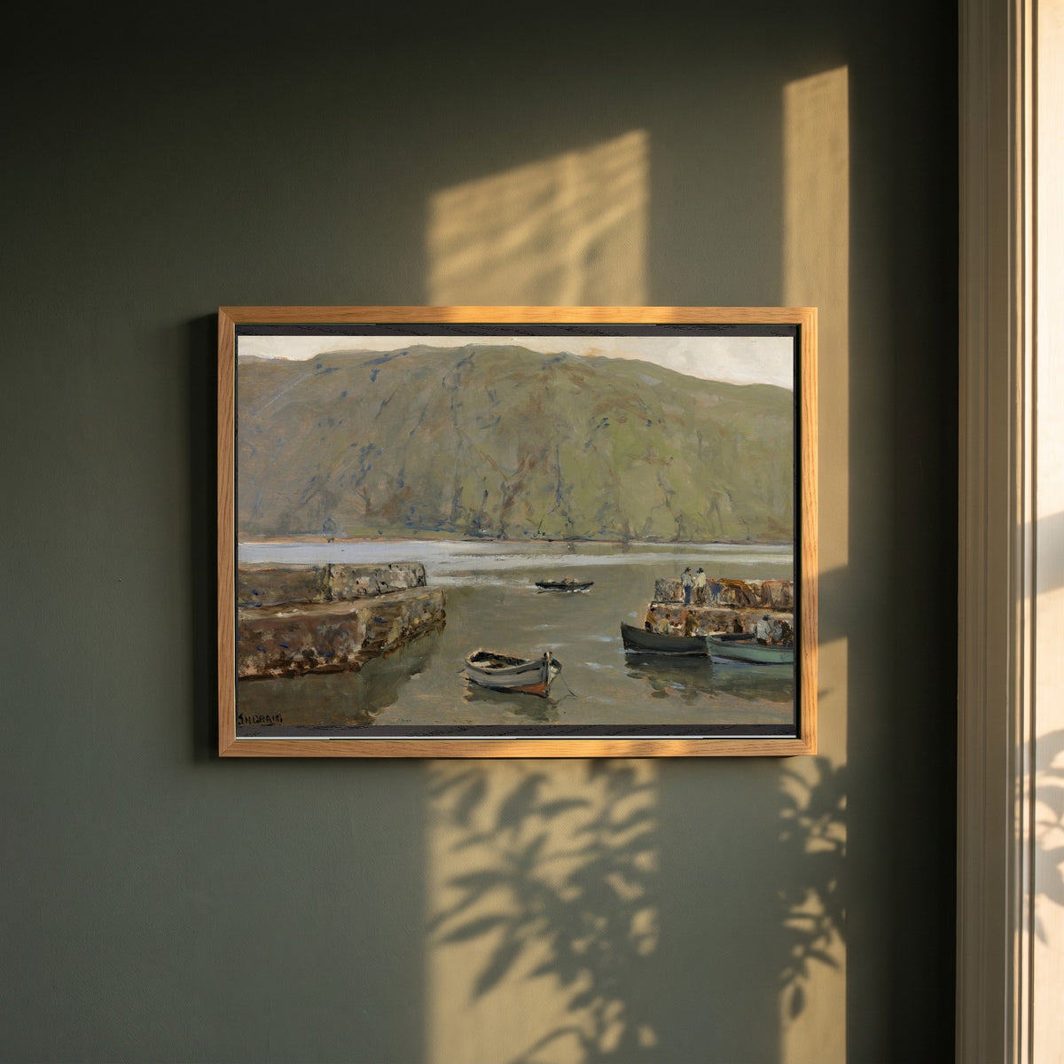 The Harbour, Leenane framed print in a natural oak frame on a dark green wall beside a window, dappled plant shadow