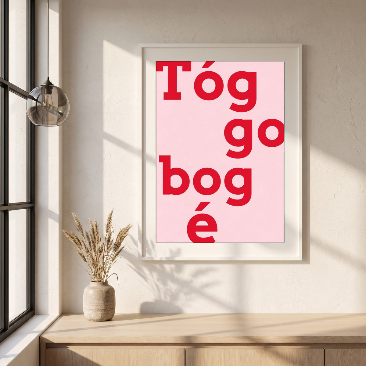 Tóg é go bog é framed print in a white frame on a plaster wall above an oak worktop in a bright Scandinavian kitchen